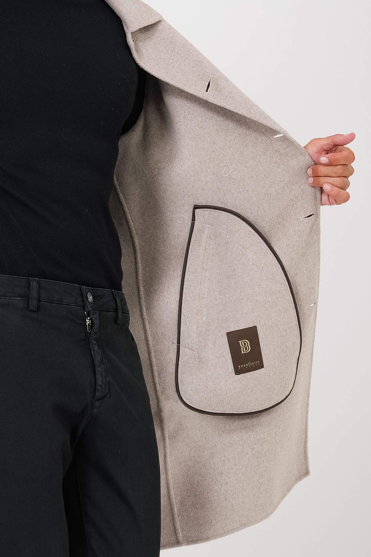 Detail of the interior of the beige coat on a model, with a piped inner pocket and logo label