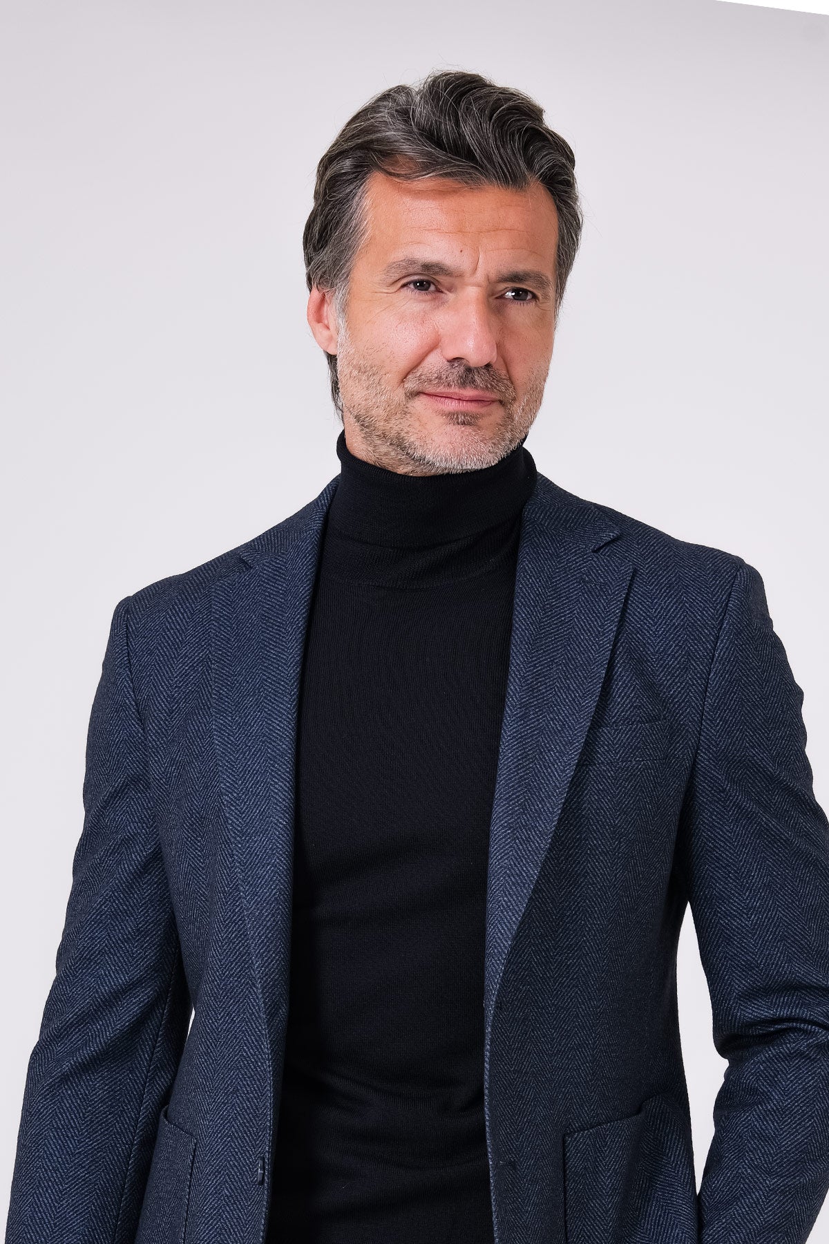 Blue herringbone jacket on a model over a roll neck, front view
