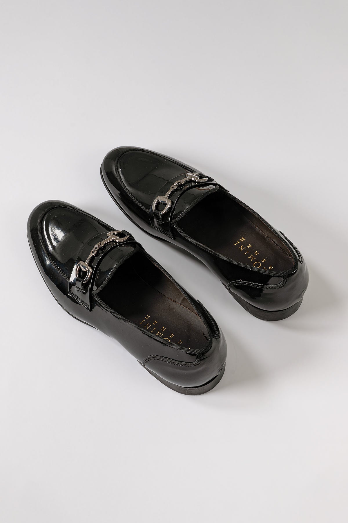 Front view of black patent leather moccasins with a decorative buckle detail