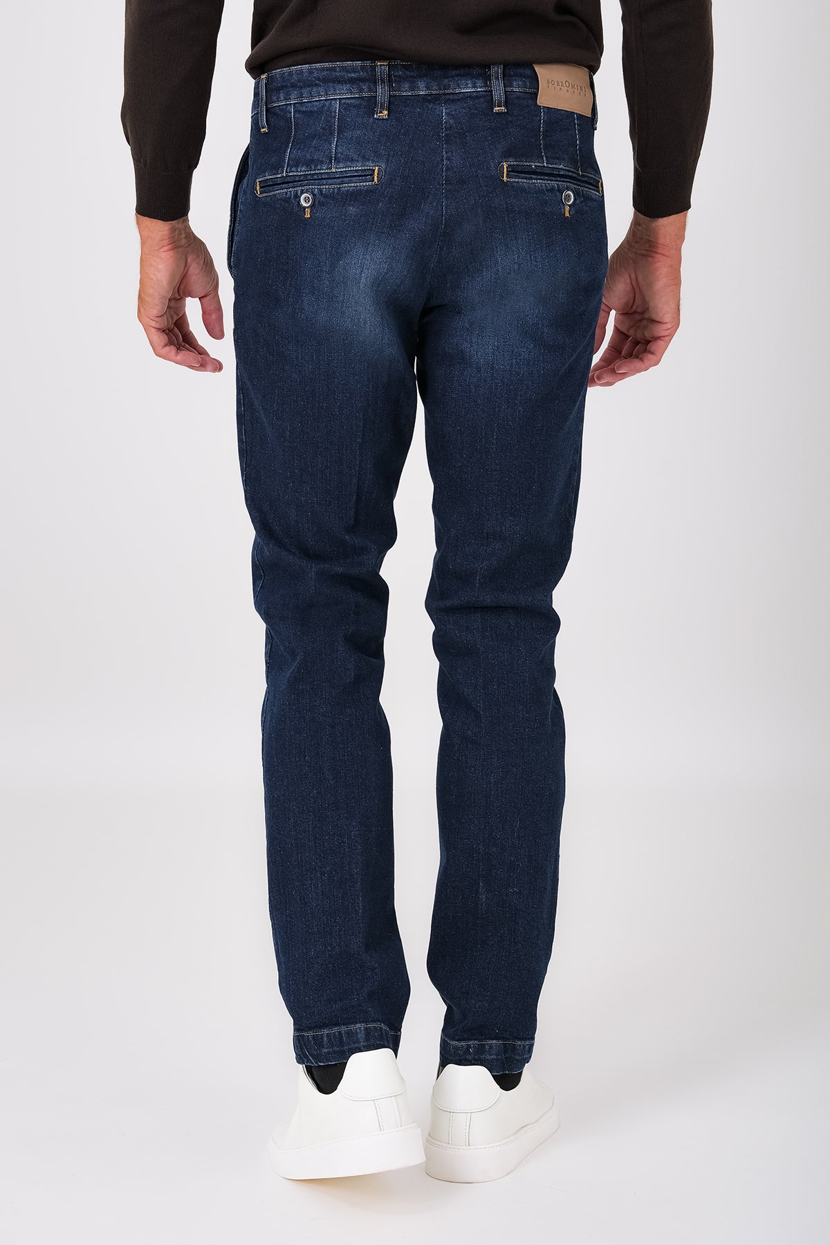 Rear view of dark denim trousers on a model, with buttoned welt pockets