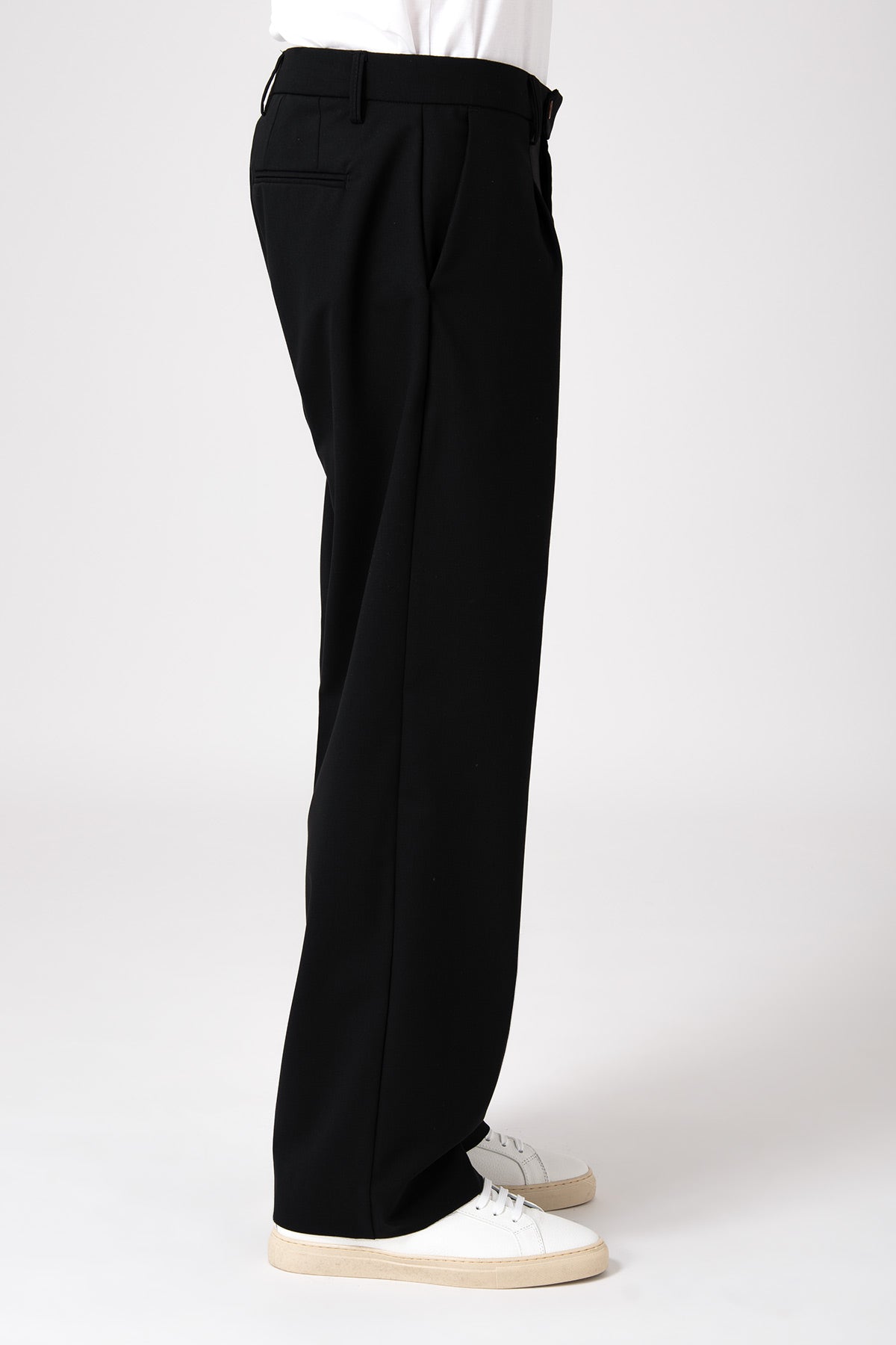 Uomo che indossa un pantalone largo nero fluido in visione laterale con scarpe bianche